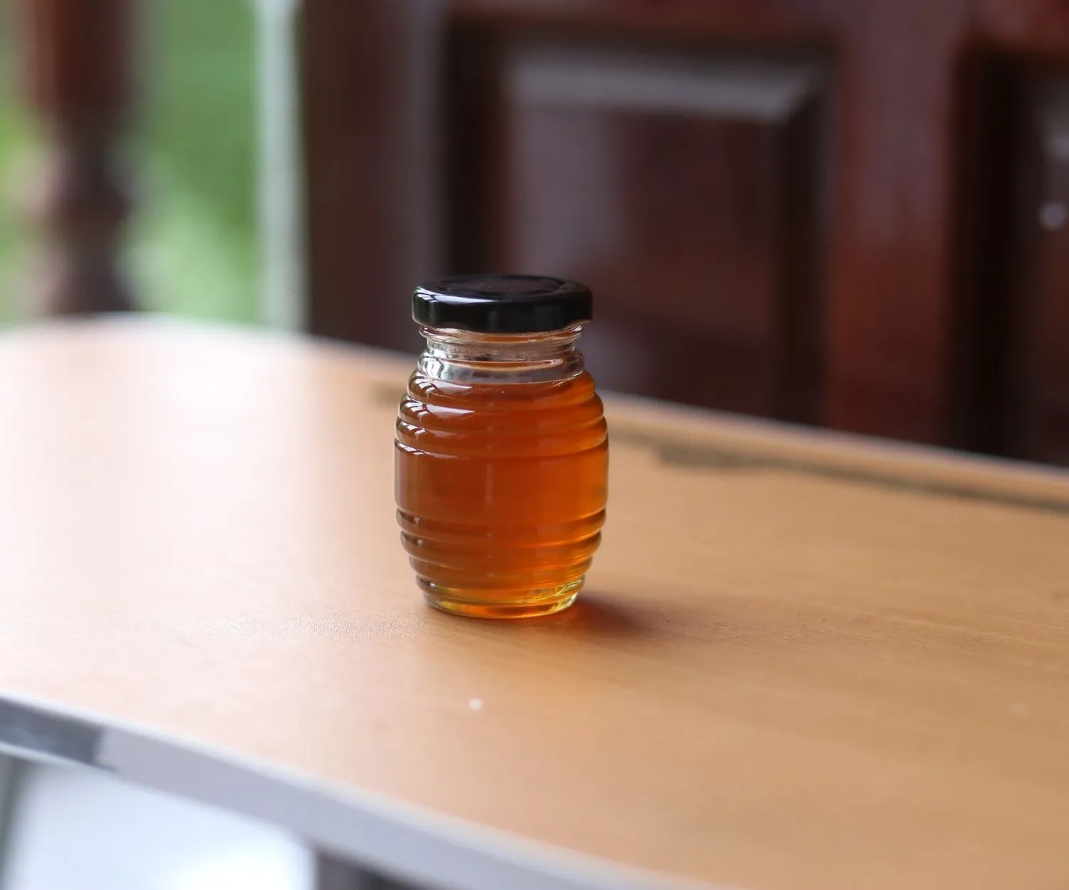 A ribbed jar of golden wildflower honey on a warm wooden table